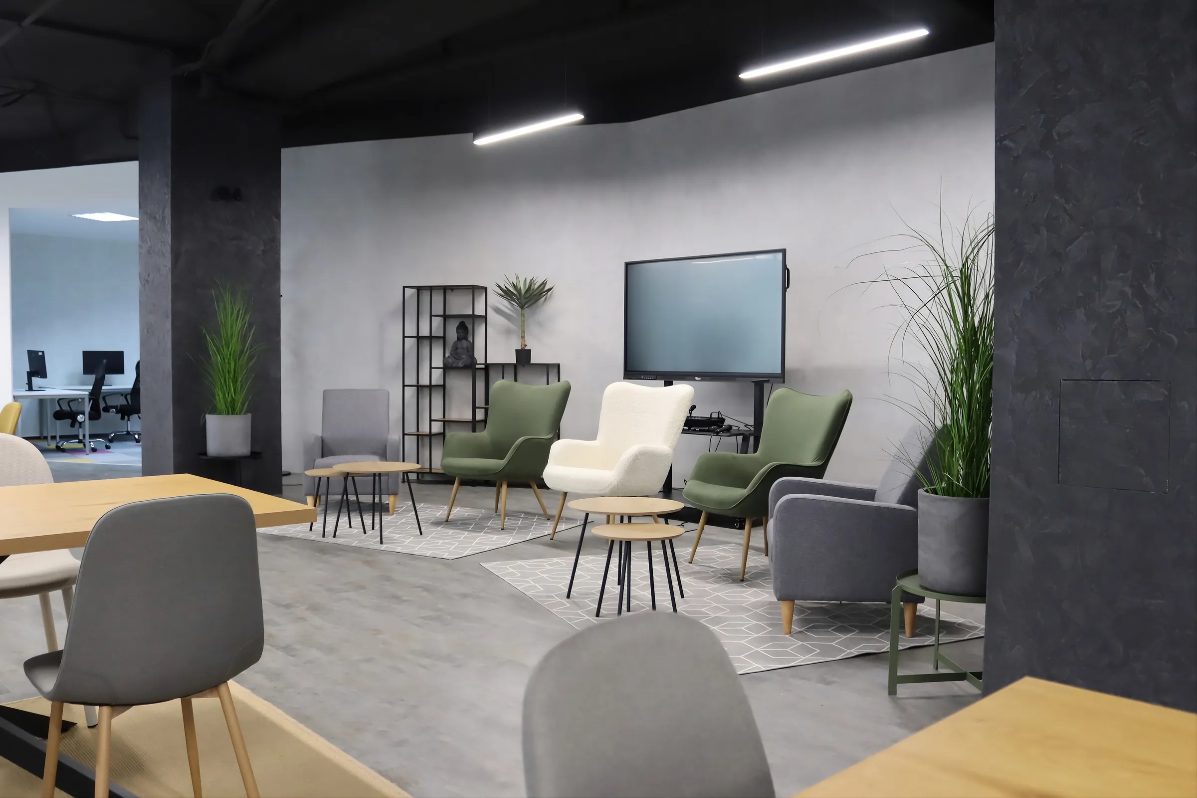 Coworkingová lounge zóna s křesly, rostlinami a velkou obrazovkou